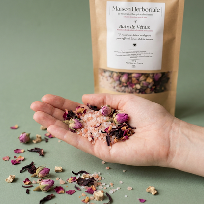 Fleurs et boutons de rose séchés dans une main, devant le paquet Bain de Vénus